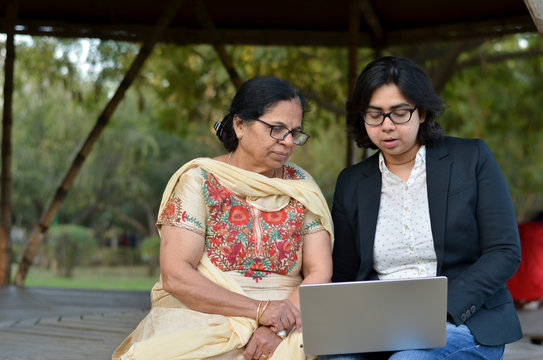 Young Indian Woman Helping Her Old Retired Mother On A Laptop Sitting In A Park In New Delhi, India Concept - Digital Literacy / Education