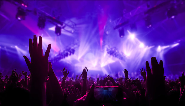 Happy people dance in nightclub DJ party concert and listen to electronic dancing music from DJ on the stage. Silhouette cheerful crowd celebrate New Year party 2020. People lifestyle DJ nightlife.