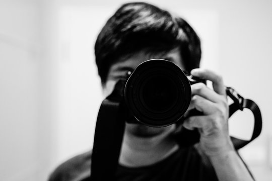 Male photographer taking selfie photo with DSLR digital camera lens closeup in mirror. Black and white view (BW)