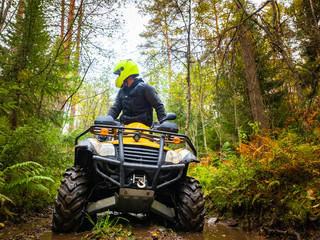 Human on the ATV. A man rides through the forest on a quad bike. Riding an ATV through mud....