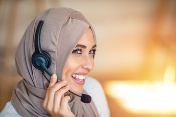 Muslim business woman with headset working in office. Happy arab woman working in company service center wearing headphone and using computer helping solving client problem