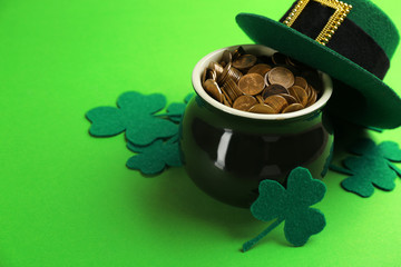 Pot of gold coins, hat and clover leaves on green background, space for text. St. Patrick's Day...