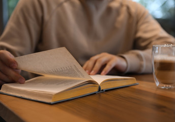 Man with coffee reading book at wooden table, closeup