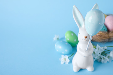 Easter bunny figure, flowers and dyed eggs on light blue background. Space for text