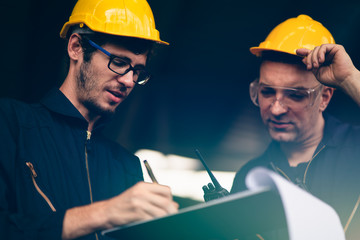 Scene of industrial workers wearing jump suit and yellow safety hat discussing the plan and operation while writing down the note on a clipboard,  Concept manufacturer quality control procedure.