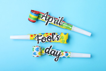 Party horns with words APRIL FOOL'S DAY on light blue background, flat lay