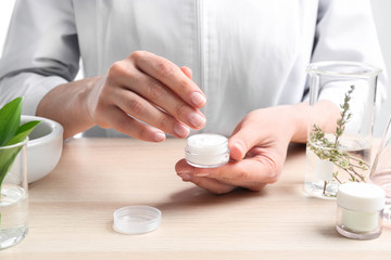 Woman with cream at table in cosmetic laboratory, closeup