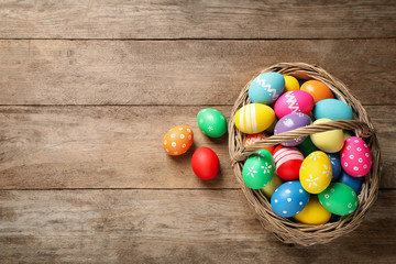 Colorful Easter eggs in basket on wooden background, flat lay. Space for text
