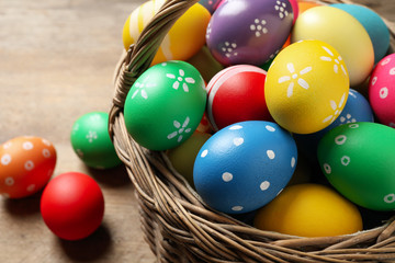 Colorful Easter eggs in basket on wooden background, closeup