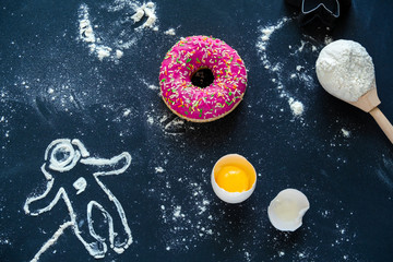 top view flat lay pink a donut , a broken egg, a spoon with flour and a silhouette of an astronaut...