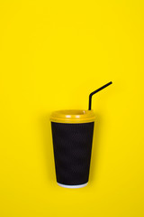 Black paper cup coffee on yellow background. Fragrant takeaway drink, layout for coffee. Business and service concept. Delicious morning drink. Bright hipster trendy design. Hard shadow. Copy space.