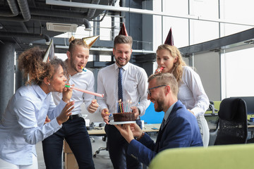 Happy business team with birthday cake are greeting colleague at office party