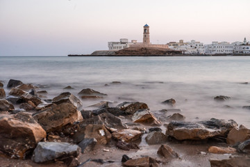 Fototapeta na wymiar Sunrise on a rocky beach with a lighthouse in the background at Sur's bay, Oman