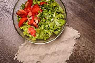 Fresh green salad with lettuce and tomatoes on wooden table. Bowl with salad