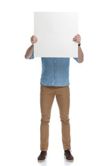 Young casual man covering his face with a blank billboard