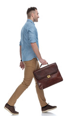 Side view of positive casual holding briefcase and smiling, stepping