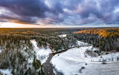 Stunning sunrise over valley surrounded with forest and river covered in snow. Scenic aerial landscape.