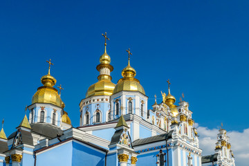 Fototapeta na wymiar Close-up of the rooftops of St Michael's Golden-Domed Cathedral in Kiev, Ukraine. The walls of the cathedral are painted blue and nicely decorated on each facade. Golden domes reflecting the sun