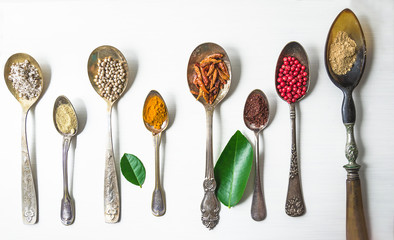 Different spices in vintage spoons on the white background. Flat lay