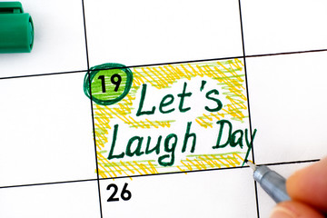 Woman fingers with pen writing reminder Lets Laugh Day in calendar.