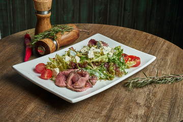 Appetizing warm salad with veal and fresh vegetables in white plate on wooden background. Healthy eating. Close up, copy space