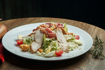 Caesar salad with croutons, parmesan, bacon, chicken, egg in black plate on wooden background. Restaurant serving. Close up with copy space. Close up
