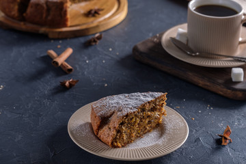 Fragrant and tasty carrot cake with a crispy crust on a plate with a cup of coffee on a dark background