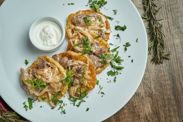 Close up view on Traditional dish of Ukrainian cuisine - potato pancakes with sour cream and beef on a white ceramic plate on rustic background