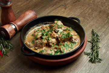 Baked potatoes with chicken in a creamy sauce in a pan on a wooden background. Close up, selective focus