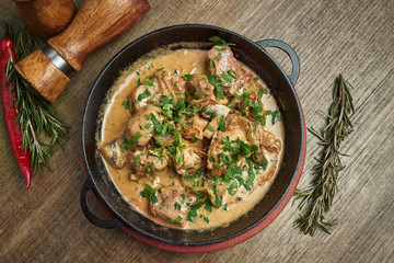 Baked potatoes with chicken in a creamy sauce in a pan on a wooden background. Top view on tasty food