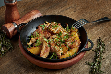 Fried potatoes with bacon, onions and herbs in a decorative pan on a wooden background. Close up, selective focus.