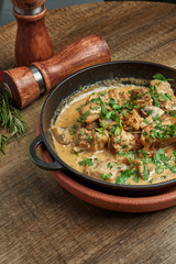 Baked potatoes with chicken in a creamy sauce in a pan on a wooden background. Close up, selective focus