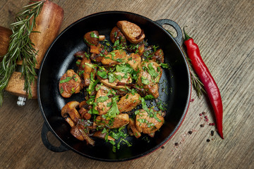 Fried potatoes with pork, onions and herbs in a decorative pan on a wooden background. Top view on tasty food.