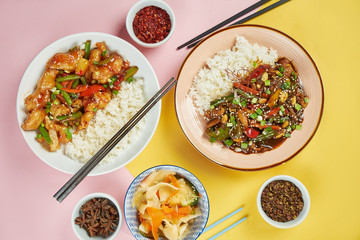 Kung Pao and chicken in sweet and sour sauce with a portion of rice in a white bowl on bright, colored background. Top view