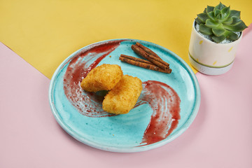 Appetizing Asian dessert - deep-fried brewed custard with milk breaded with raspberry sauce on a blue plate on a colored background. Youtiao. Deep Fried Milk