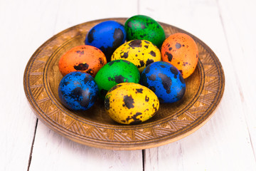 Multicolored easter eggs in a plate on a white wooden background.