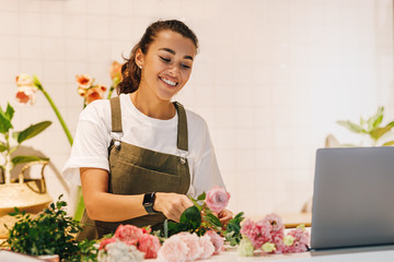 Smiling woman working in her flower shop. Female florist arranging flowers on the counter.