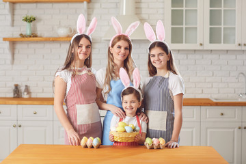 Fototapeta premium Happy easter. Mother and daughters with rabbit ears decorate Easter eggs at a table in kitchen.