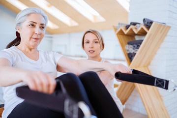 Personal trainer assist senior woman exercising on machine at gym