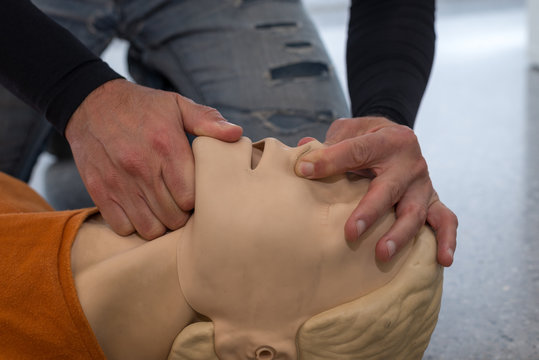 Man teaching cardiopulmonary resuscitation with a dummy on a white background. Opening airways and covering the nose to prepare air insufflations.