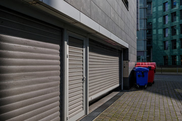 View of metal roller shutter doors and metal door at service area of office buildings with roll of plastic waste garbage container bin.