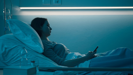 Sleepless patient lying in bed and chatting with her smartphone