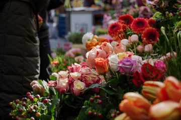 Moody dark tone. Selected focus view at pale orange, pink and white bouquet of blooming roses in front of floral shop in outdoor market in Europe. Typical atmosphere of flower store.   