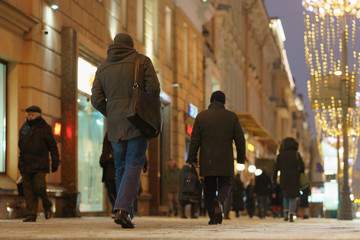 People on the city street in downtown district. Rear view. Street is illuminated brightly.