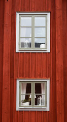 Fototapeta na wymiar Old red plank wood swedish cottage windows with white frame. Curtains and laps in the windows