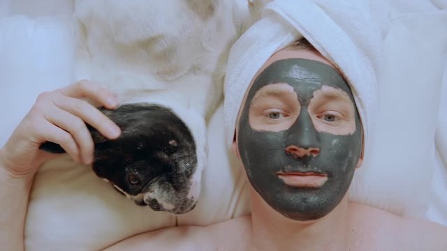 close up man with cosmetic mask on face lying on the pillow with french bulldog beauty treatment