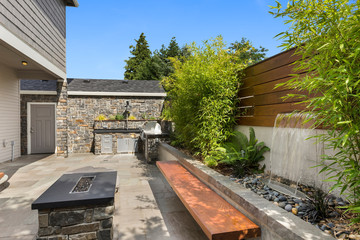 Home exterior backyard hardscape entertainment area with fire pit, bench seating, water feature and...