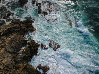 Aerial top view of sea waves hitting rocks on the beach with turquoise sea water. Amazing rock cliff seascape in the Portuguese coastline. Drone shot.