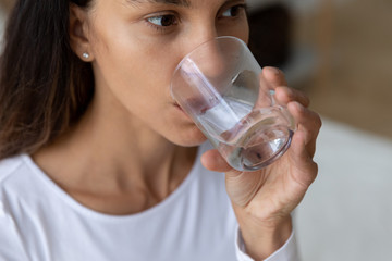 Close up of young Caucasian woman hold glass drinking pure mineral water maintain body balance, millennial girl enjoy clear still aqua fell thirsty at home, healthy lifestyle, good habit concept