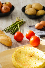 Potato omelette as a typical Spanish dish along with different healthy and vegetarian ingredients such as tomatoes, onions, eggs or asparagus, accompanied by a handmade loaf of bread, selective focus